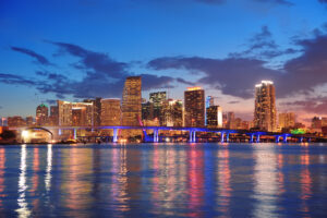 Miami city skyline panorama at dusk with urban skyscrapers and bridge over sea with reflection